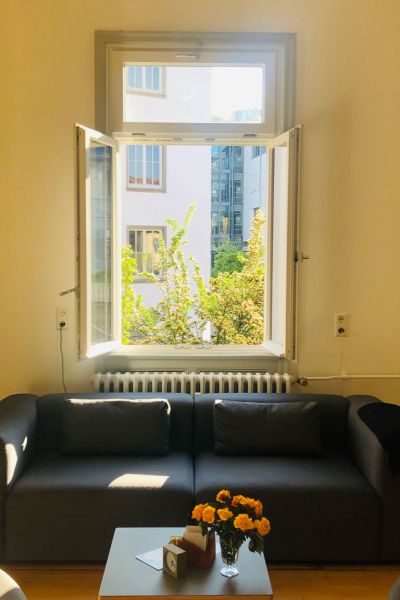 Sofa mit Blumenvase auf Beistelltisch vor geöffnetem Fenster